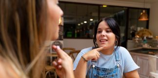 Two young women drinking coffee, talking in sign language. Deaf friends or couple communicating, having fun, pleasant conversation, sitting together